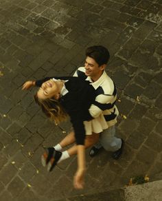 a man and woman walking down a street next to each other with their arms around each other