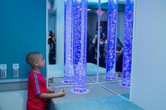 a young boy standing in front of a mirror with blue lights on the walls and floor