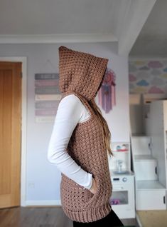 a woman wearing a hooded vest and hoodie standing in a kitchen with her back turned to the camera