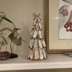 a small tree made out of shells sitting on top of a mantle next to a bird