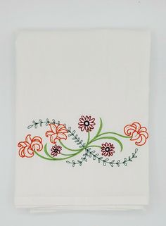 a white towel with red and orange flowers embroidered on the front, sitting on a table