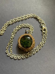 a necklace with a green glass cabochon hanging from it's chain on a gray surface