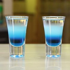 two glasses filled with blue liquid sitting on top of a table