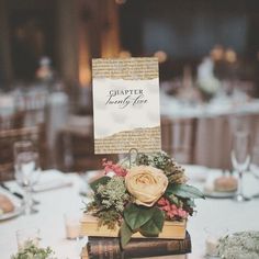 a table topped with books covered in flowers and greenery next to a centerpiece