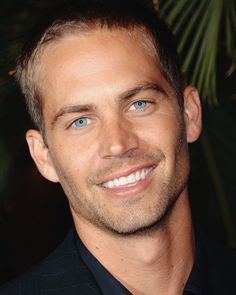 a close up of a person wearing a suit and smiling at the camera with palm trees in the background