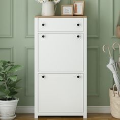 a white cabinet sitting next to a potted plant