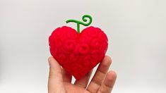 a hand holding a red heart shaped object with a green t on it's tip