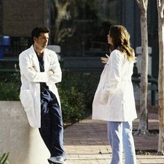 a man and woman standing next to each other on a sidewalk with trees in the background