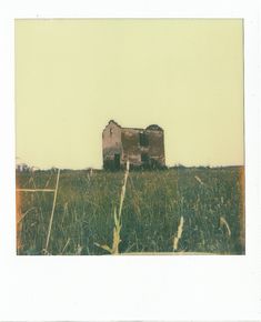 an old abandoned house sitting on top of a grass covered hill in the middle of nowhere