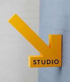 a yellow sign on the side of a building that says studio next to a white brick wall