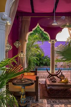 an outdoor living area with pink walls and white columns, potted plants, and wicker furniture