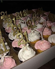 cupcakes with pink frosting and gold numbers are in a box on the table