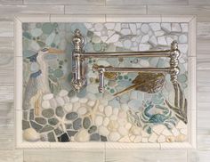 a mosaic tile wall with a bird and sea shells in the center, along with two faucets