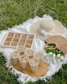 a picnic blanket on the grass with cups and trays filled with food sitting on top of it