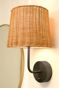 a lamp that is on the side of a wall next to a mirror with a wicker shade