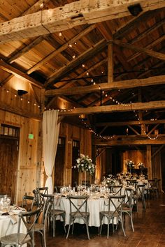 the inside of a barn with tables and chairs set up for a formal dinner or reception