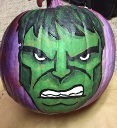 a green and purple pumpkin with an angry face painted on it's front side