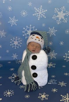 a newborn baby wearing a snowman hat and scarf is posed in front of some snowflakes