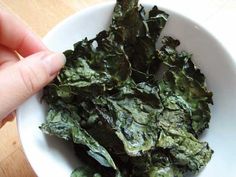 a white bowl filled with greens on top of a wooden table next to a person's hand