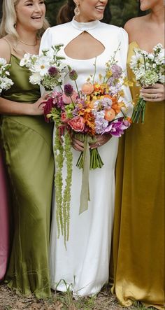 three women standing next to each other in dresses and holding bouquets smiling at the camera