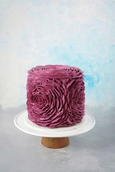 a pink cake sitting on top of a white plate next to a blue wall and wooden stand