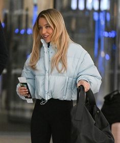 a woman walking down the street while holding onto a cell phone and carrying a black bag