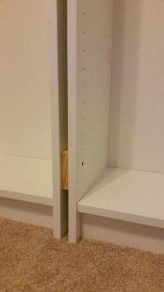 two white shelving units in a room with carpeted flooring and beige walls