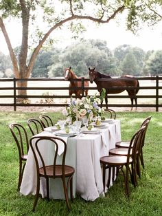 the table is set with white linens and flowers in front of two brown horses