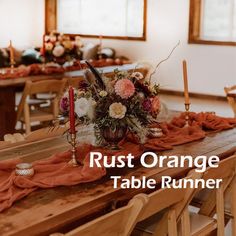 an orange table runner with flowers and candles on it in the middle of a dining room