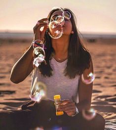 a woman sitting in the sand blowing bubbles