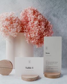 pink flowers are in a white vase next to a card and wooden stand with the label table 8