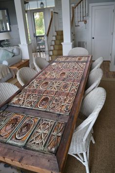 a large wooden table sitting inside of a living room next to white chairs and a stair case