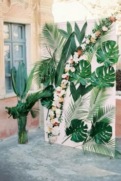 two vases filled with flowers and greenery next to a large wall decoration on the side of a building