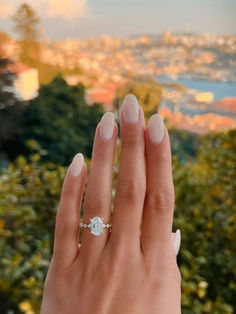 a woman's hand with a diamond ring on it and trees in the background