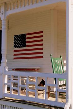 an american flag painted on the side of a white house with a dog in front