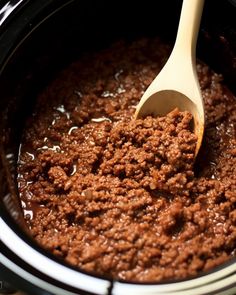 a wooden spoon in a slow cooker filled with ground beef and chili sauce, ready to be cooked