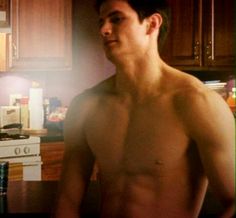 a man without a shirt standing in a kitchen