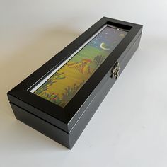 an open box with a painting inside on a white tablecloth covered floor and the lid is black