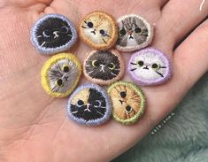 a person's hand is holding six small embroidered patches with different cats on them