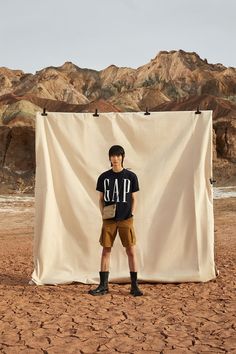 a man standing in front of a white backdrop with mountains behind him and wearing black boots