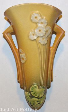 a yellow vase with flowers painted on the front and sides, hanging from a wall