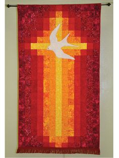 a quilted wall hanging with a bird on it's side and a cross in the middle