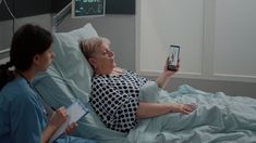 two women in hospital gowns are looking at a cell phone while laying on a bed