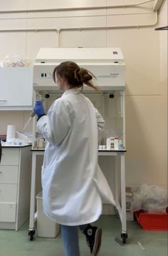 a woman in white lab coat and blue pants standing next to a counter with laboratory equipment on it