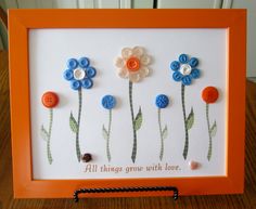 an orange frame with buttons and flowers on the inside, saying all things grow with love