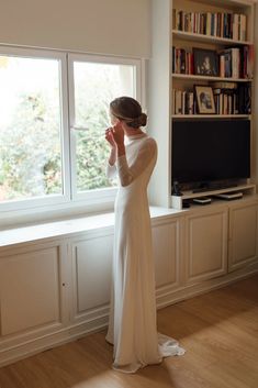 a woman standing in front of a window next to a book shelf with books on it