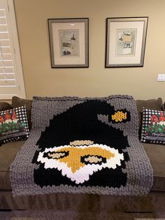 a crocheted blanket with an eagle on it sitting on a couch in front of two framed pictures