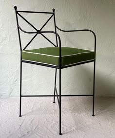 a green chair sitting on top of a white floor next to a wall with an iron frame