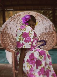 a woman sitting in a wicker chair next to a pool wearing a pink flowered dress