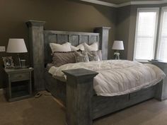 a large bed sitting next to two lamps on either side of a window in a bedroom